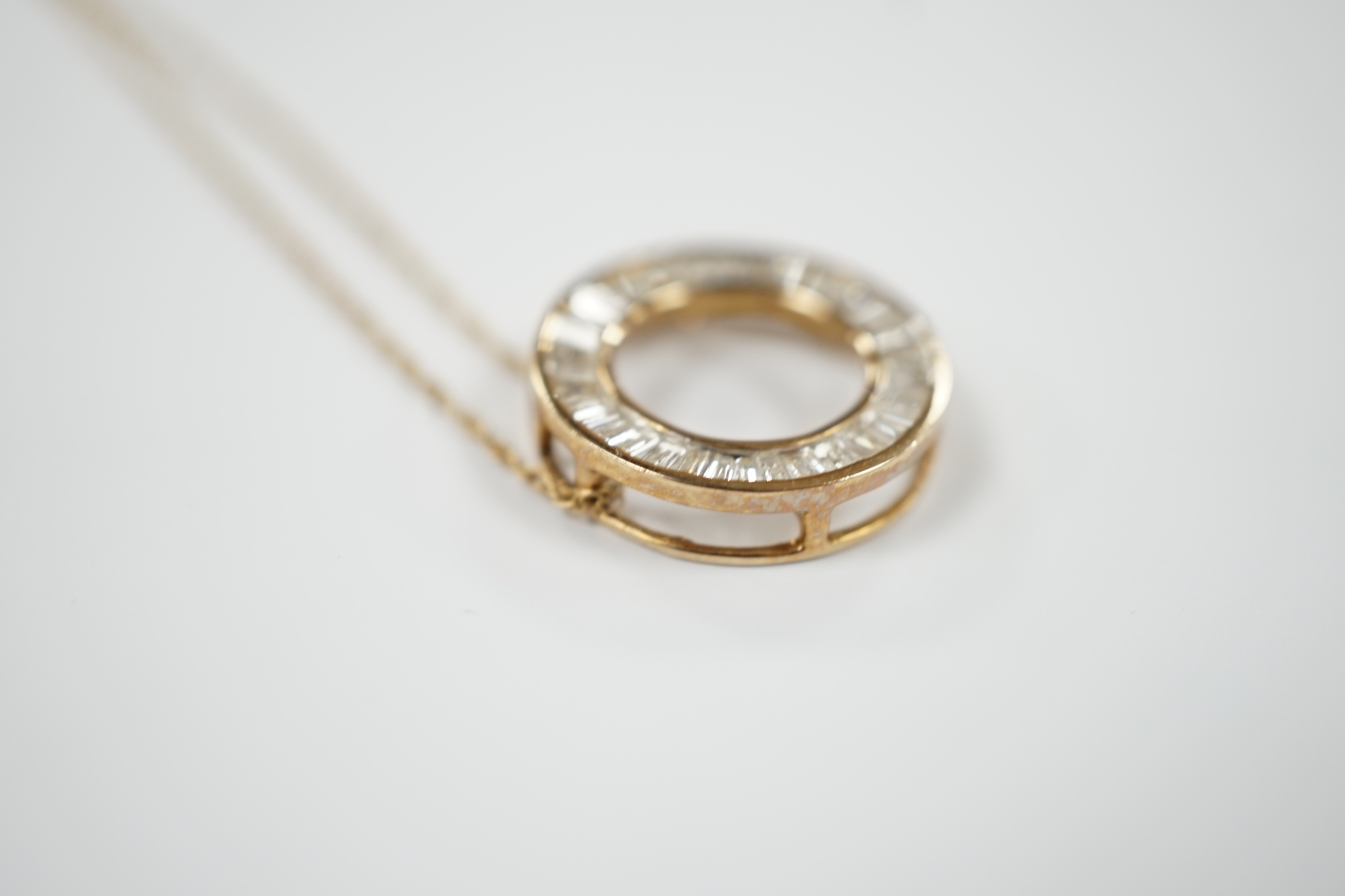 A yellow metal and trapeze cut diamond cluster set wheel pendant, 17mm, on a 9k fine link chain, 44cm, gross weight 2.1 grams.